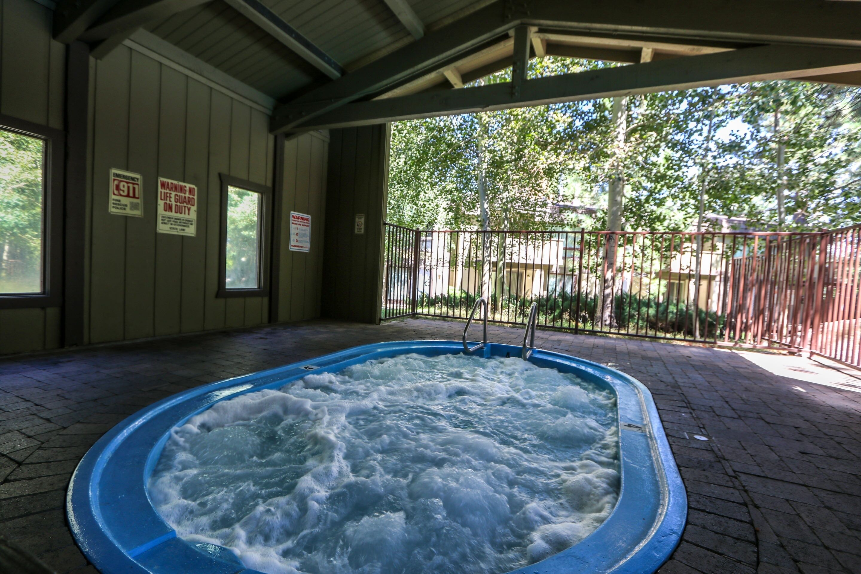 A hot tub with a metal railing, surrounded by a brick floor and a covered area with a metal roof.