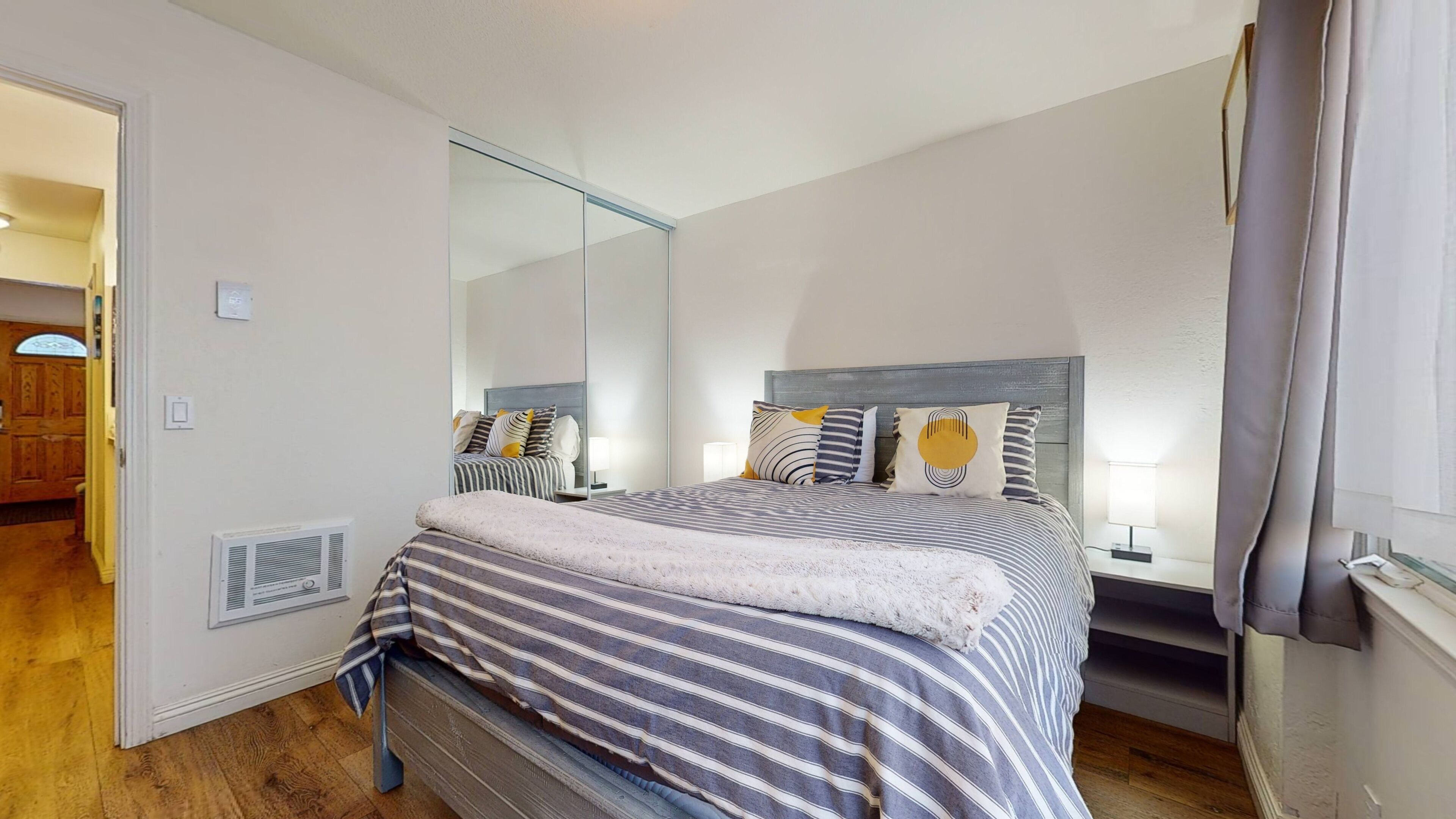 Une chambre à coucher avec un lit, un grand miroir, des lampes de chevet et un plancher en bois.