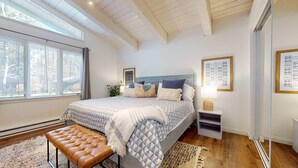 A bedroom with a large bed, a bench, a nightstand with a lamp, and framed artwork on the walls.
