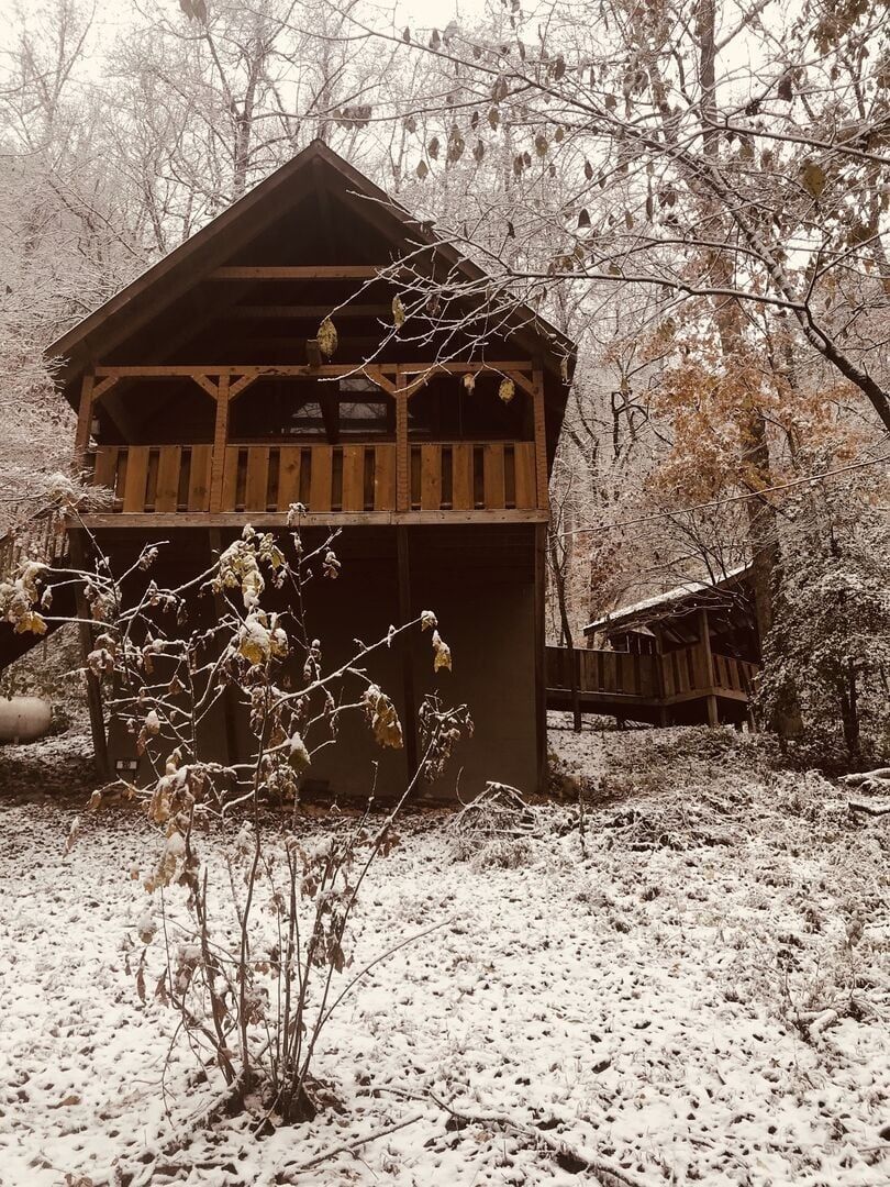 A wooden cabin with a balcony, surrounded by snow-covered ground and trees.