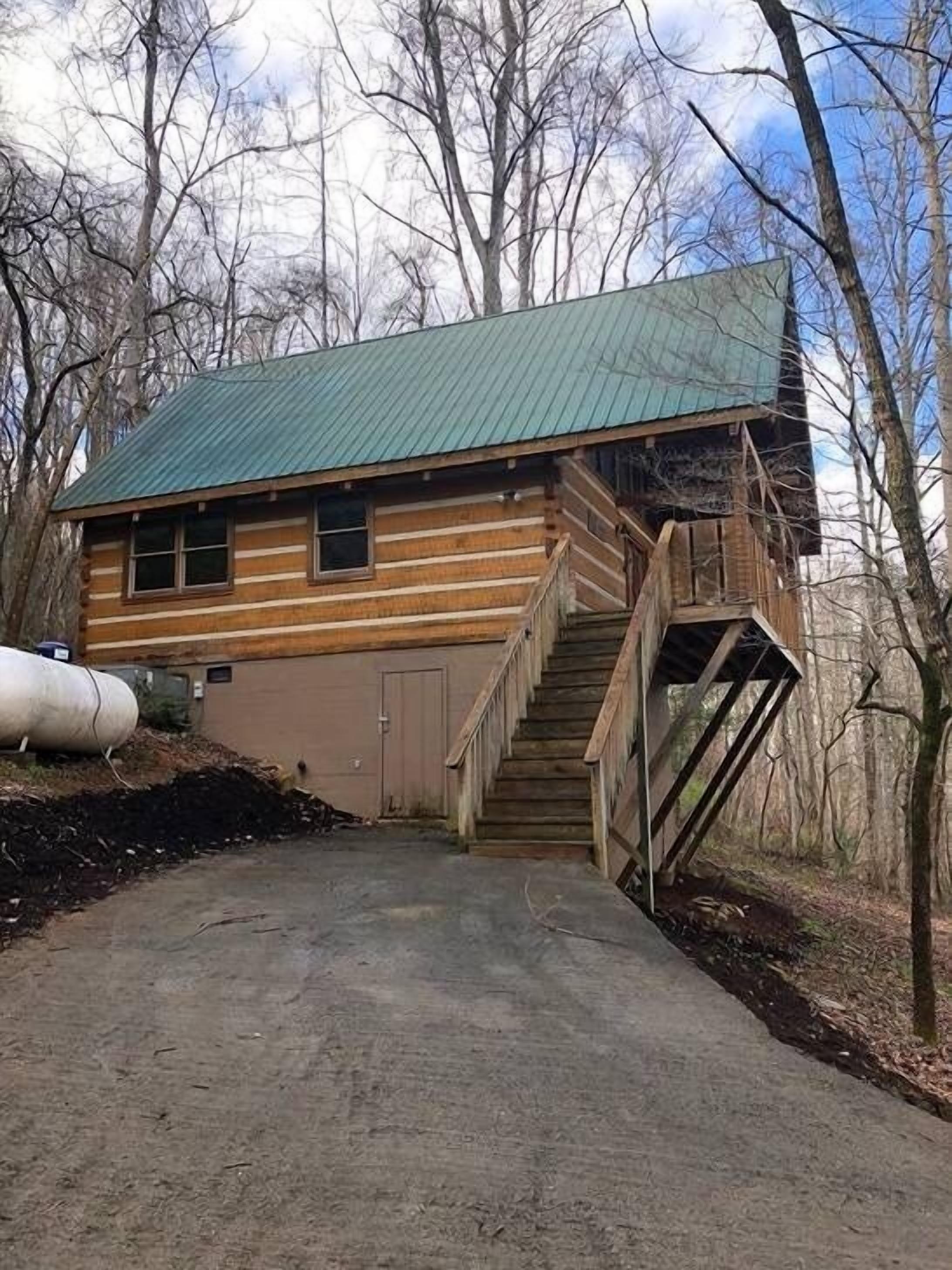 A log cabin with a metal roof, a wooden staircase, and a concrete driveway.
