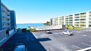 A parking lot with a view of the ocean, a building with multiple floors, and a white car parked in the lot. - Thunder Island 112c 2 Bedroom Condo by RedAwning (Ocean City)