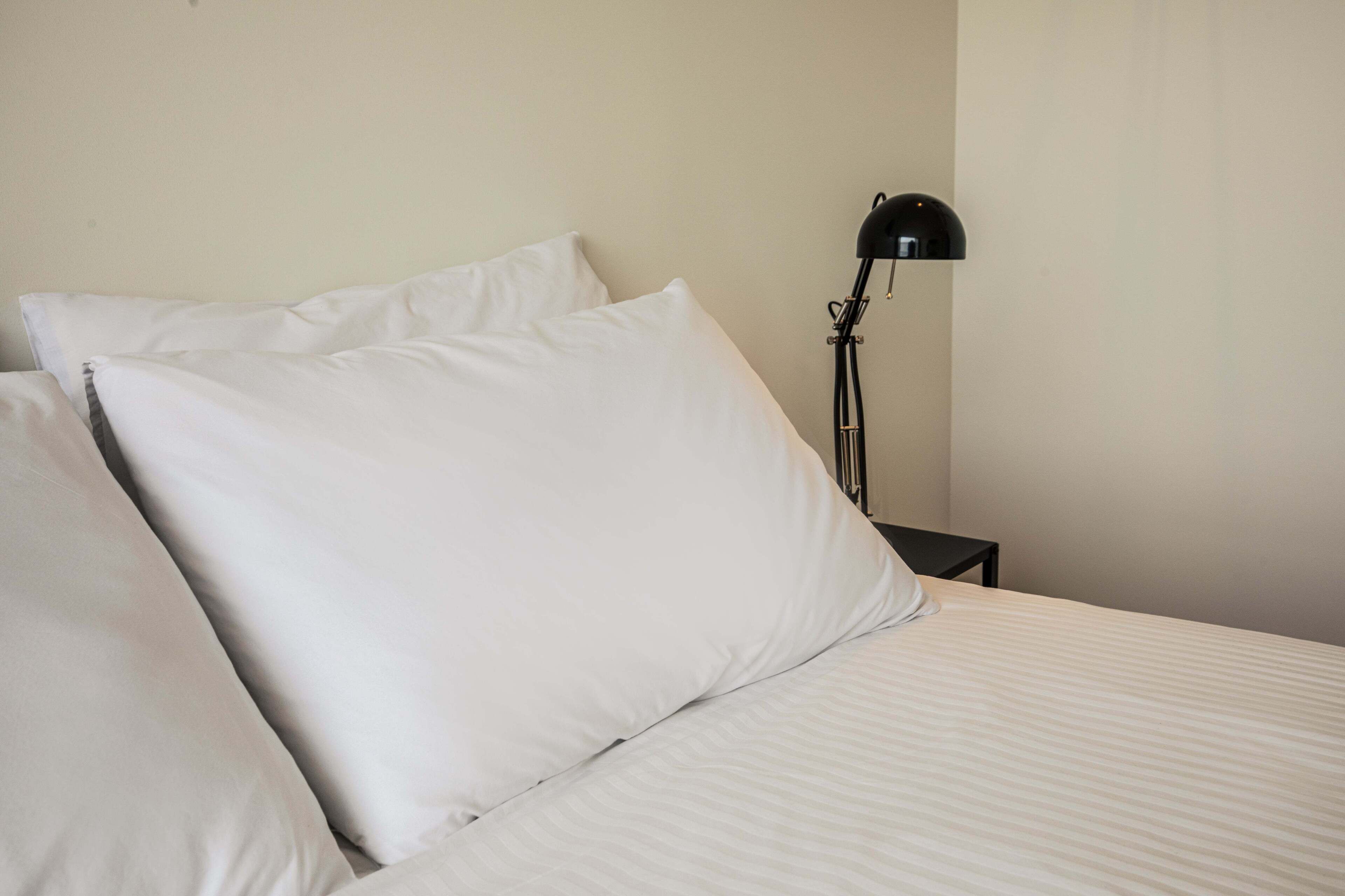 A bed with white linens and a black floor lamp.