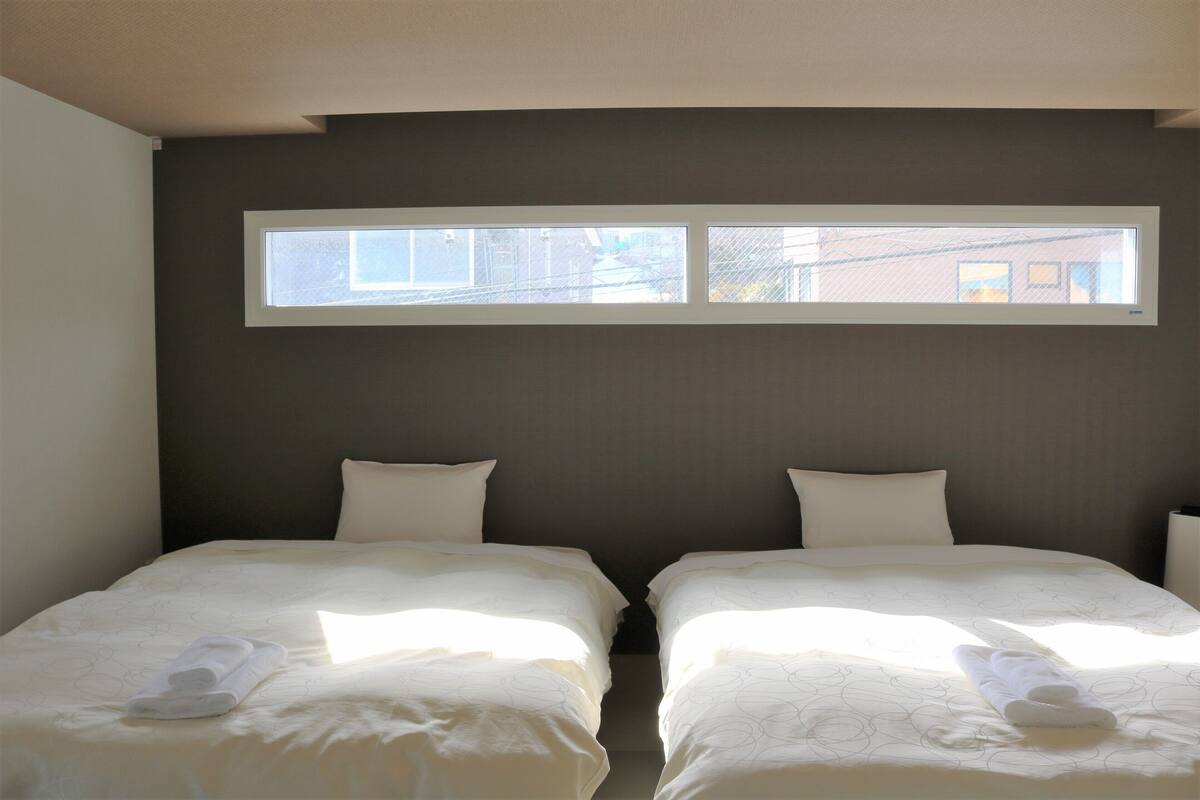 A twin room with two beds, a window, and a view of buildings outside.