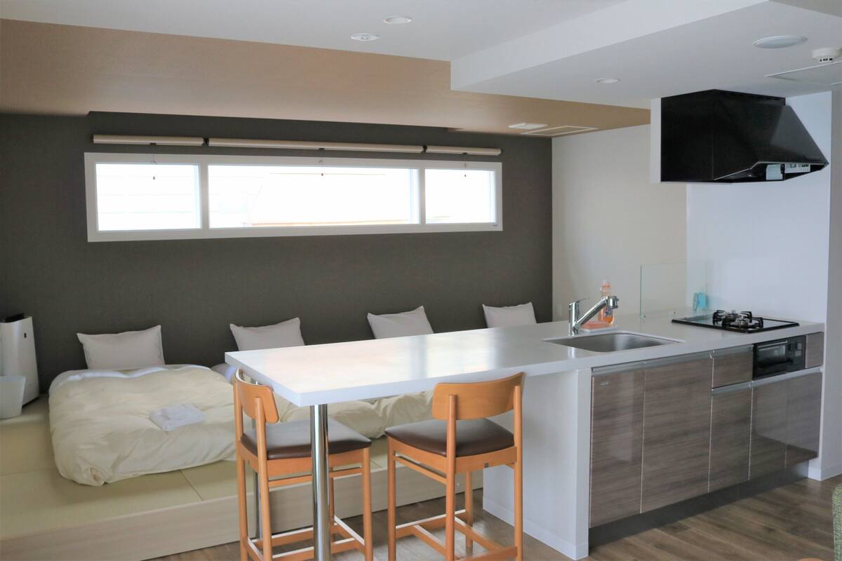 A modern kitchen with a central island, bar stools, a built-in oven, and a window above the sink.