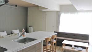 A modern kitchen with a sink, a dining area with a table and chairs, a sofa, and a window with curtains. - Stay's OTARU (Otaru)