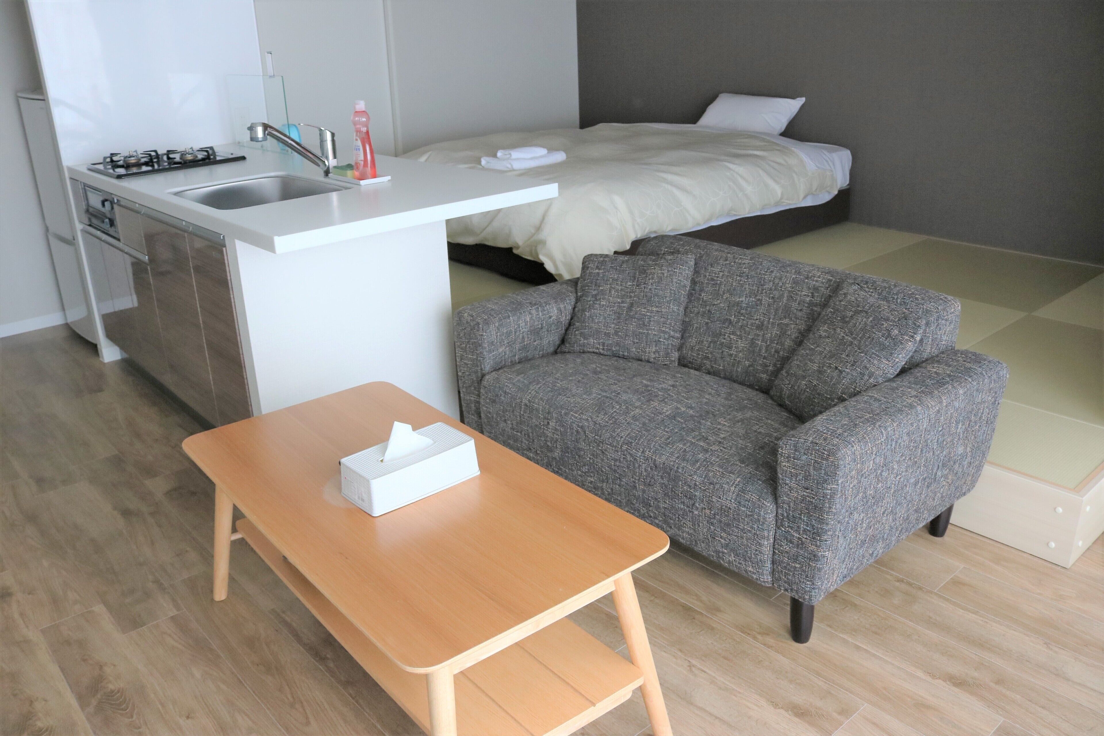 A compact hotel room with a kitchenette, a sofa, a small wooden table, and a bed.