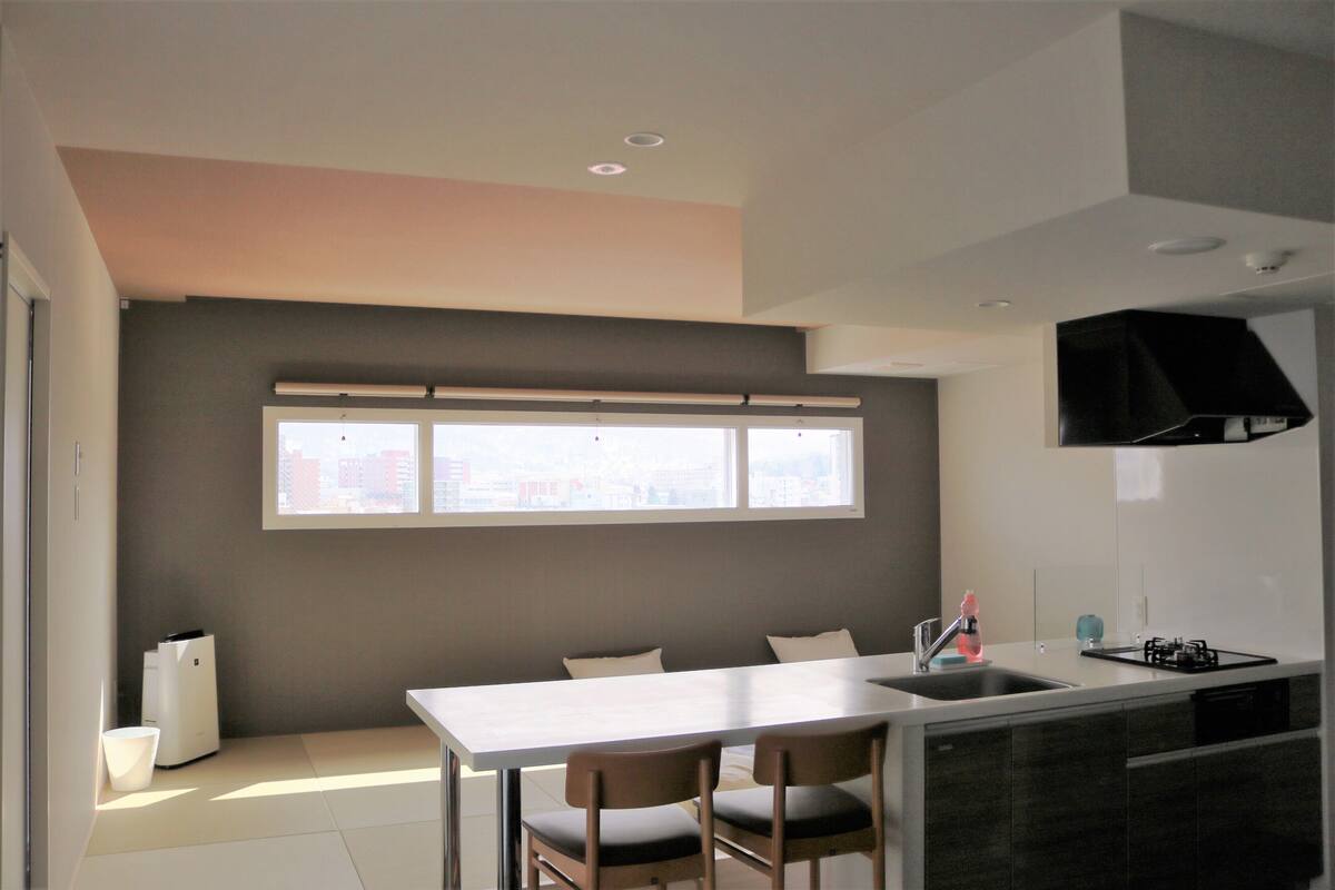 A modern kitchen with a large window, a dining area with two chairs, and a built-in stove.