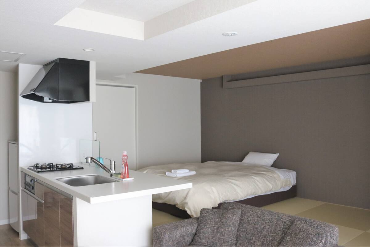 A modern hotel room with a kitchenette, a bed, and a seating area.