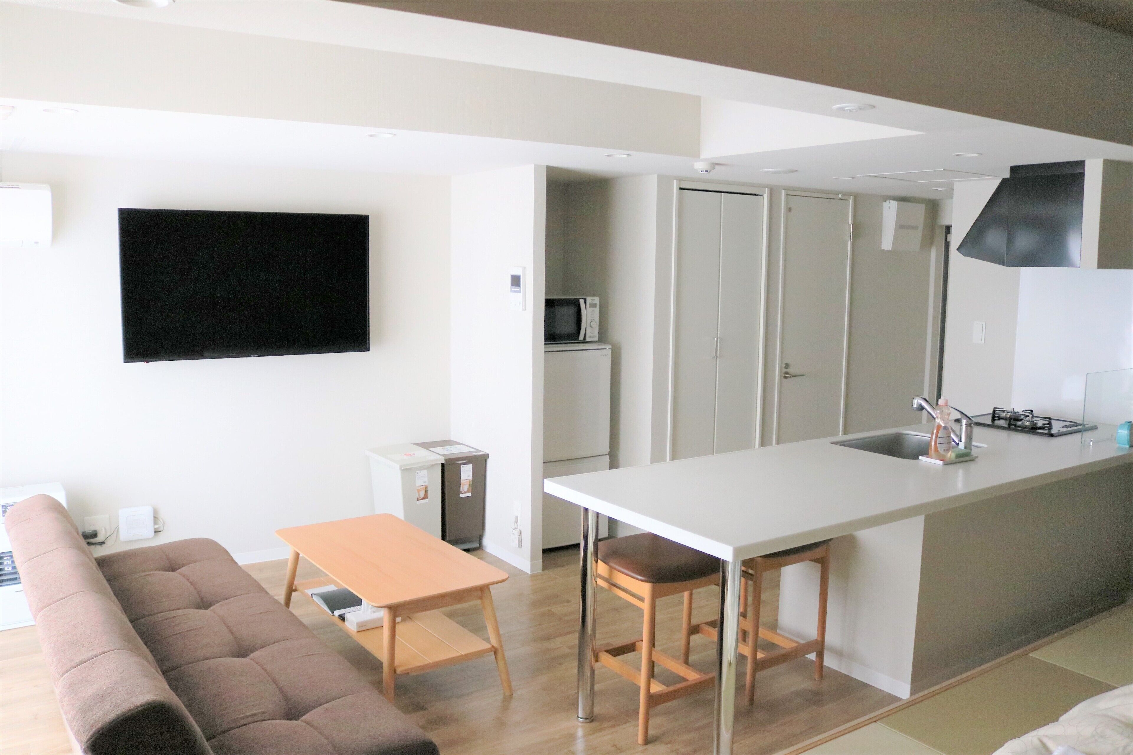Una cocina moderna con una isla central, un área de comedor con un sofá y un televisor montado en la pared.