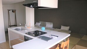 A compact kitchenette with a gas stove, sink, and a small dining area with two chairs. - Stay's OTARU (Otaru)