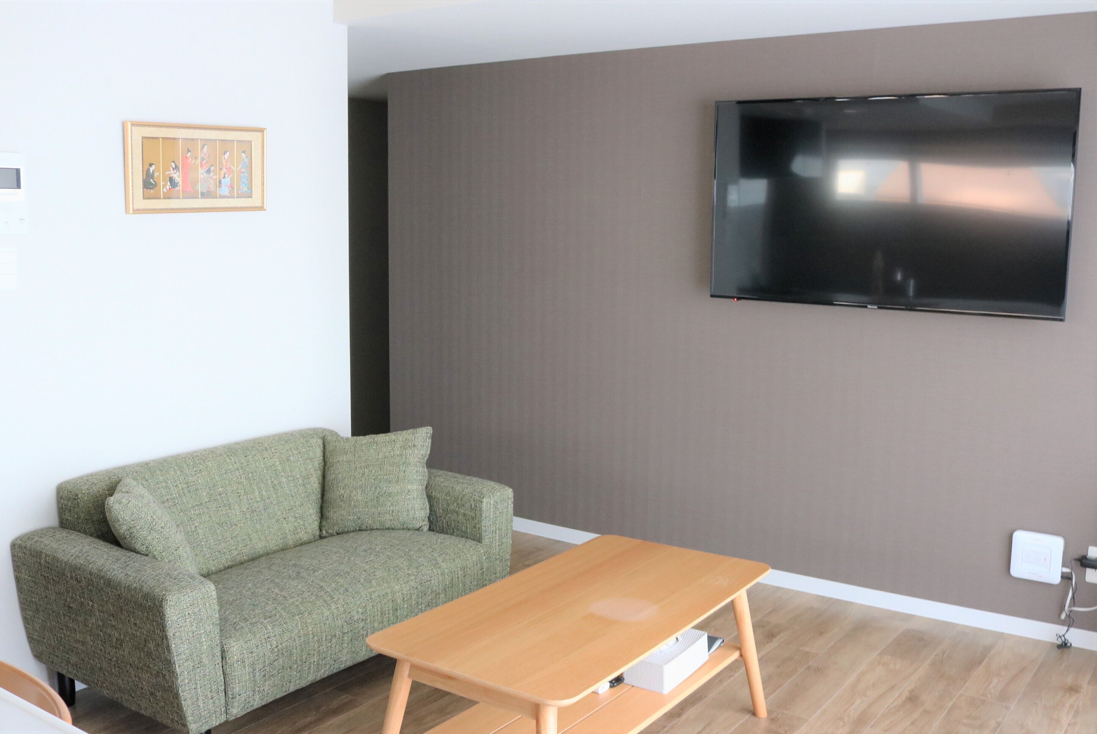A living room with a green sofa, a wooden coffee table, a flat-screen TV mounted on the wall, and a framed picture on the wall.