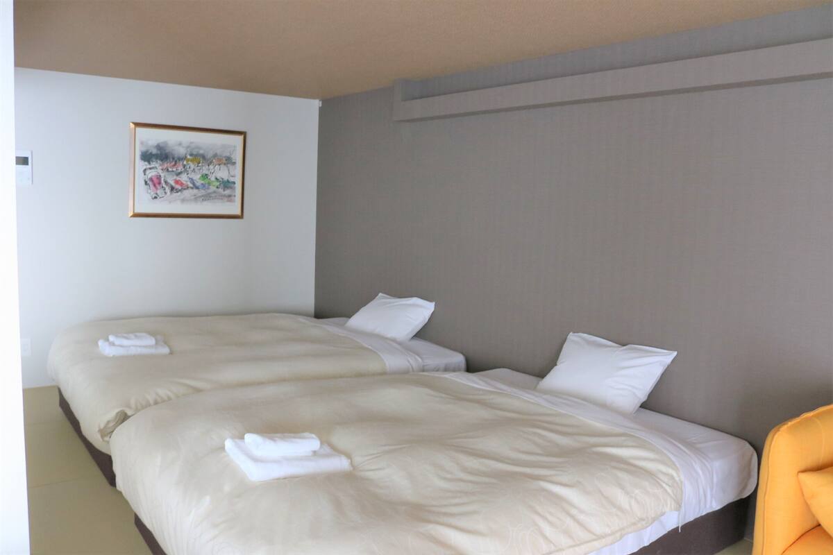 A hotel room with two beds, a painting on the wall, and a chair.