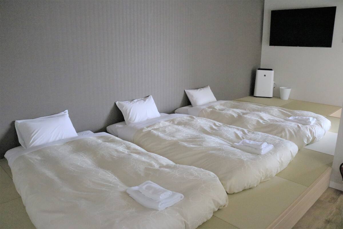 A hotel room with two beds, each with white bedding and pillows. There is a small table with a white cup and a device on it.