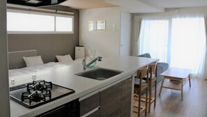 A modern kitchen with a gas stove, sink, and wooden chairs. - Stay's OTARU (Otaru)