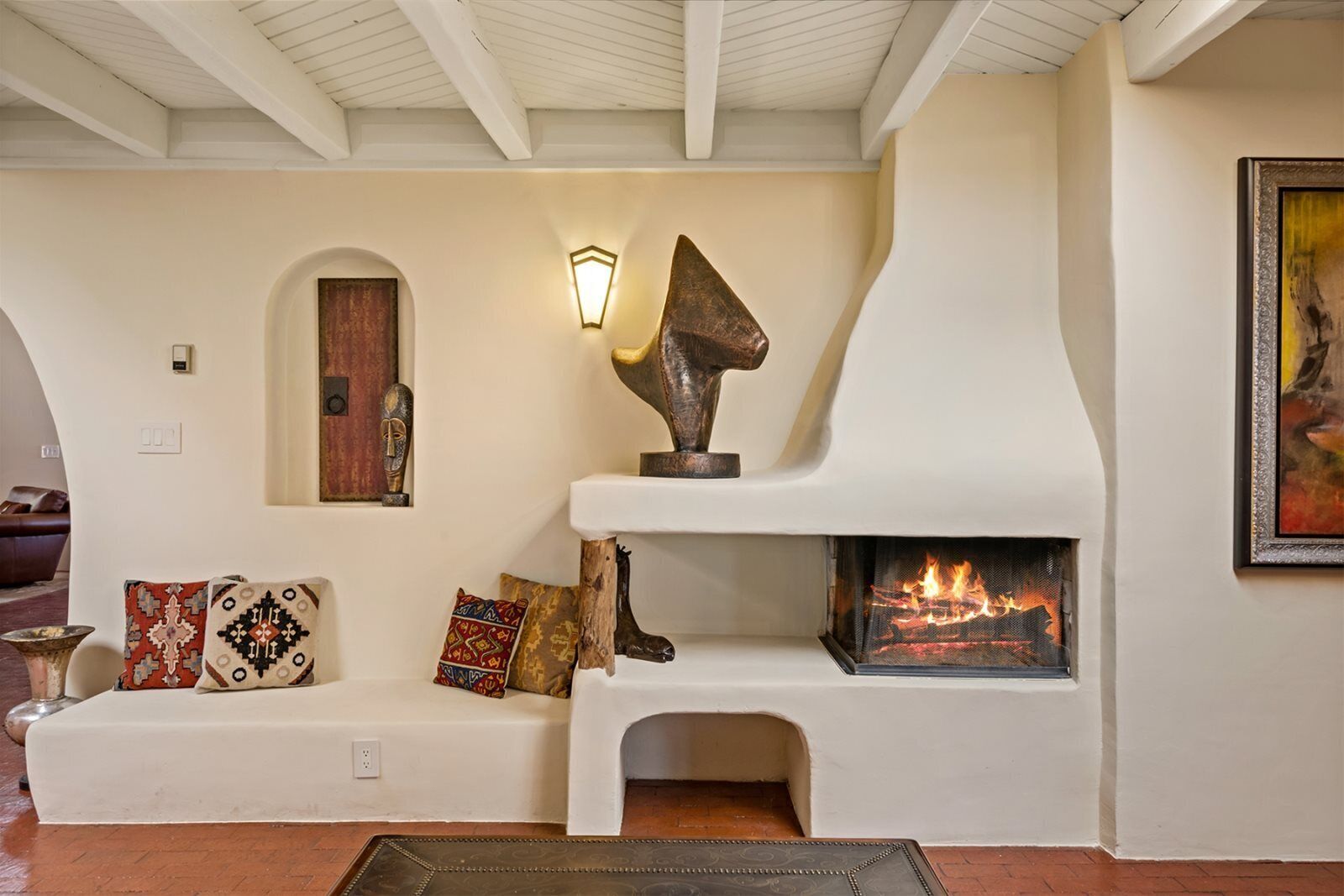 A cozy living room with a fireplace, a bench with cushions, and a wall-mounted light fixture.