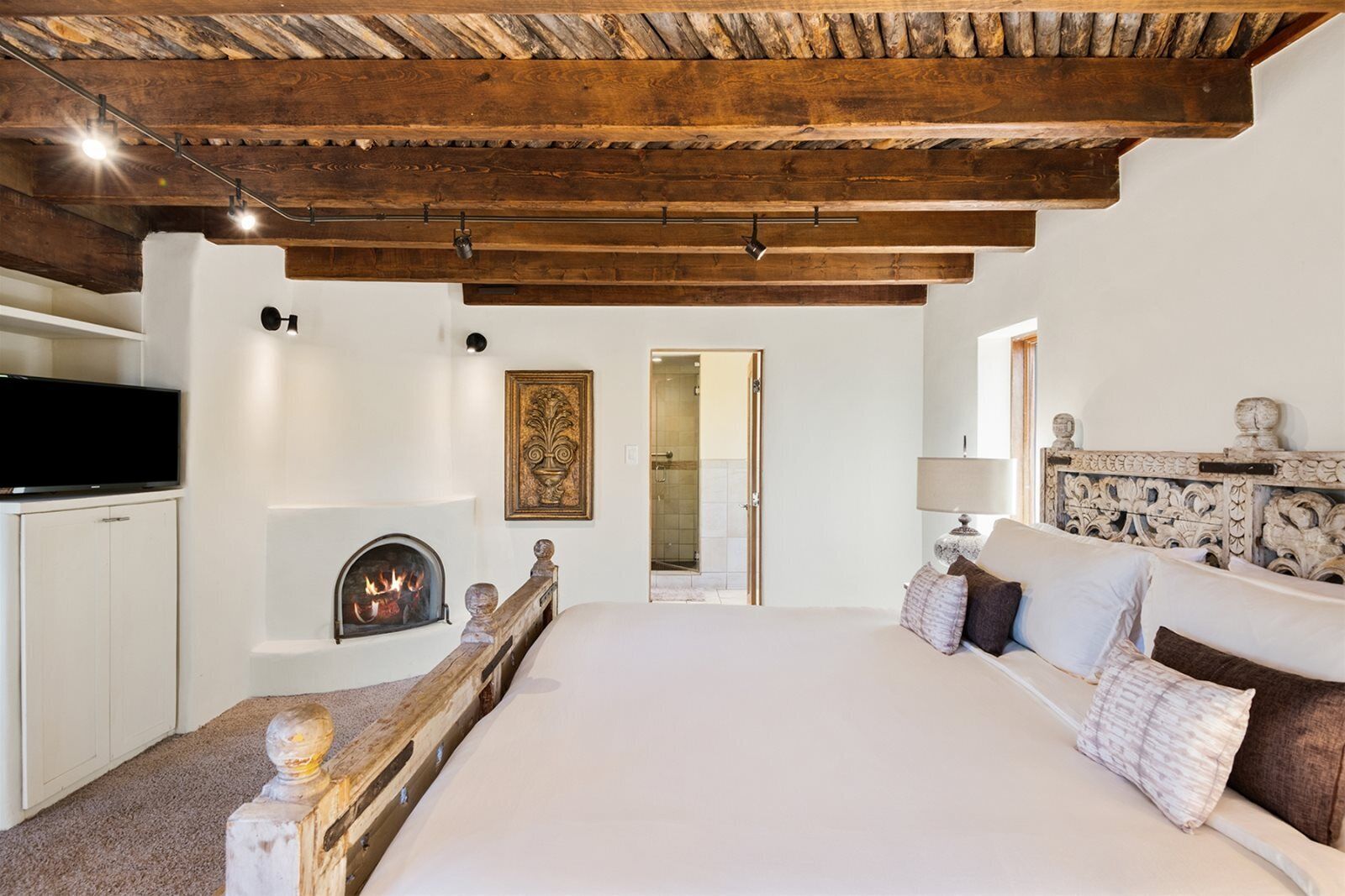 A bedroom with a large bed, a fireplace, a TV, and a wooden ceiling.