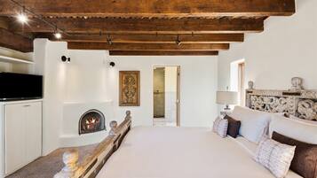 A bedroom with a large bed, a fireplace, a TV, and a wooden ceiling.