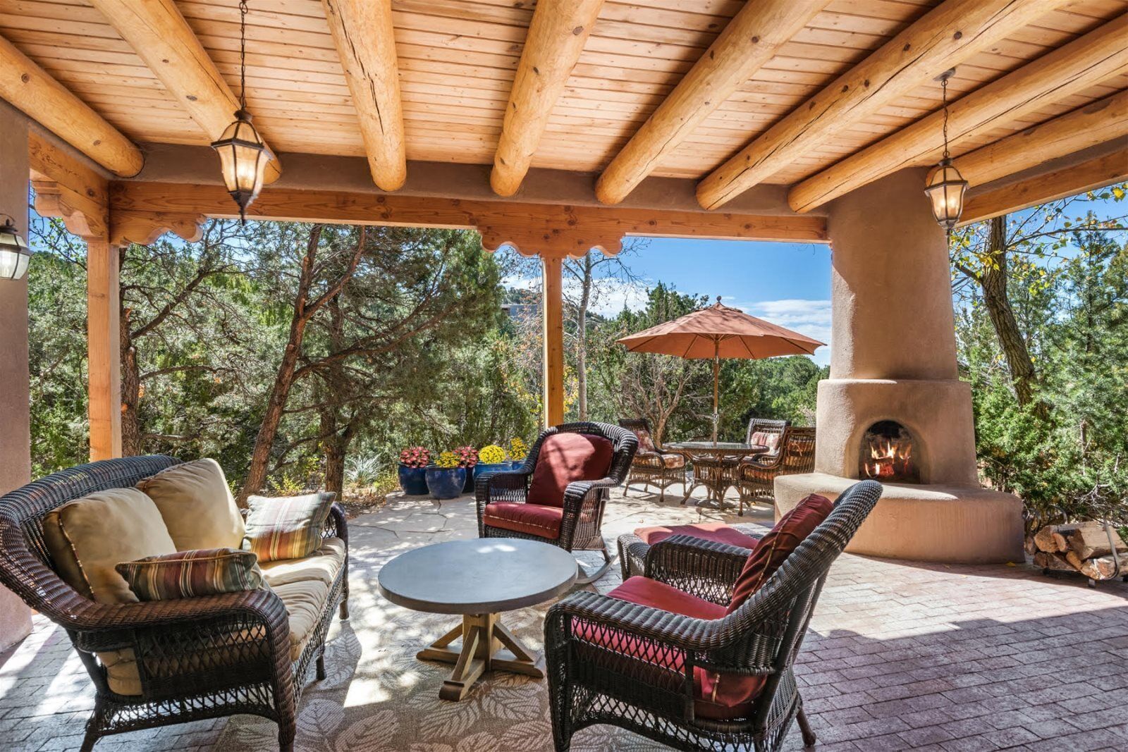 Ein überdachter Patio-Bereich mit Korbmöbeln, einem runden Tisch und einem Feuerkorb.