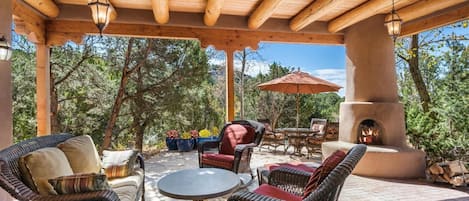 Ein überdachter Patio-Bereich mit Korbmöbeln, einem runden Tisch und einem Feuerkorb.