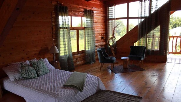 A log cabin bedroom with a bed, two chairs, a lamp, and large windows. - Stunning Cabin w/360º view of Guatemala Highlands (Tecpán Guatemala)
