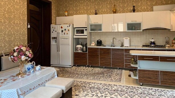 A modern kitchen with a central island, built-in appliances, and a dining area with a table set for two. - Sitorabonu-Guest House (Tashkent)
