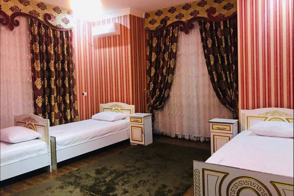 A room with two single beds, each with a nightstand and a lamp. The room has striped curtains and a patterned headboard.