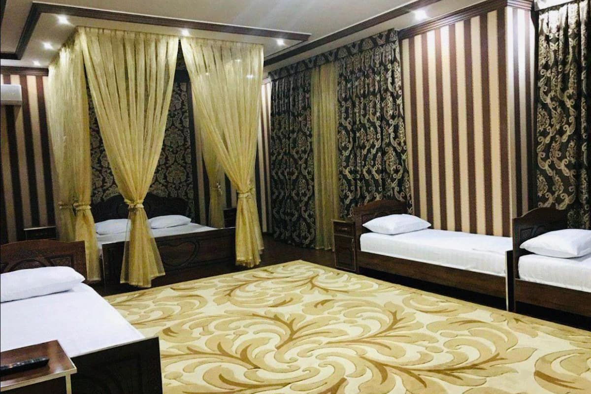 A hotel room with two single beds, a large patterned carpet, and curtains with a paisley design.