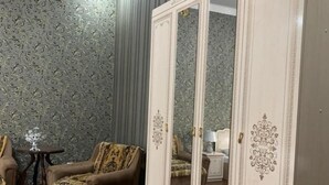 A room with a patterned wallpaper, a large white wardrobe, a red carpet, and a small round table with a lamp. - Sitorabonu-Guest House (Tashkent)