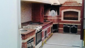 A compact kitchen with a gas stove, oven, and a brick oven. - Sitorabonu-Guest House (Tashkent)