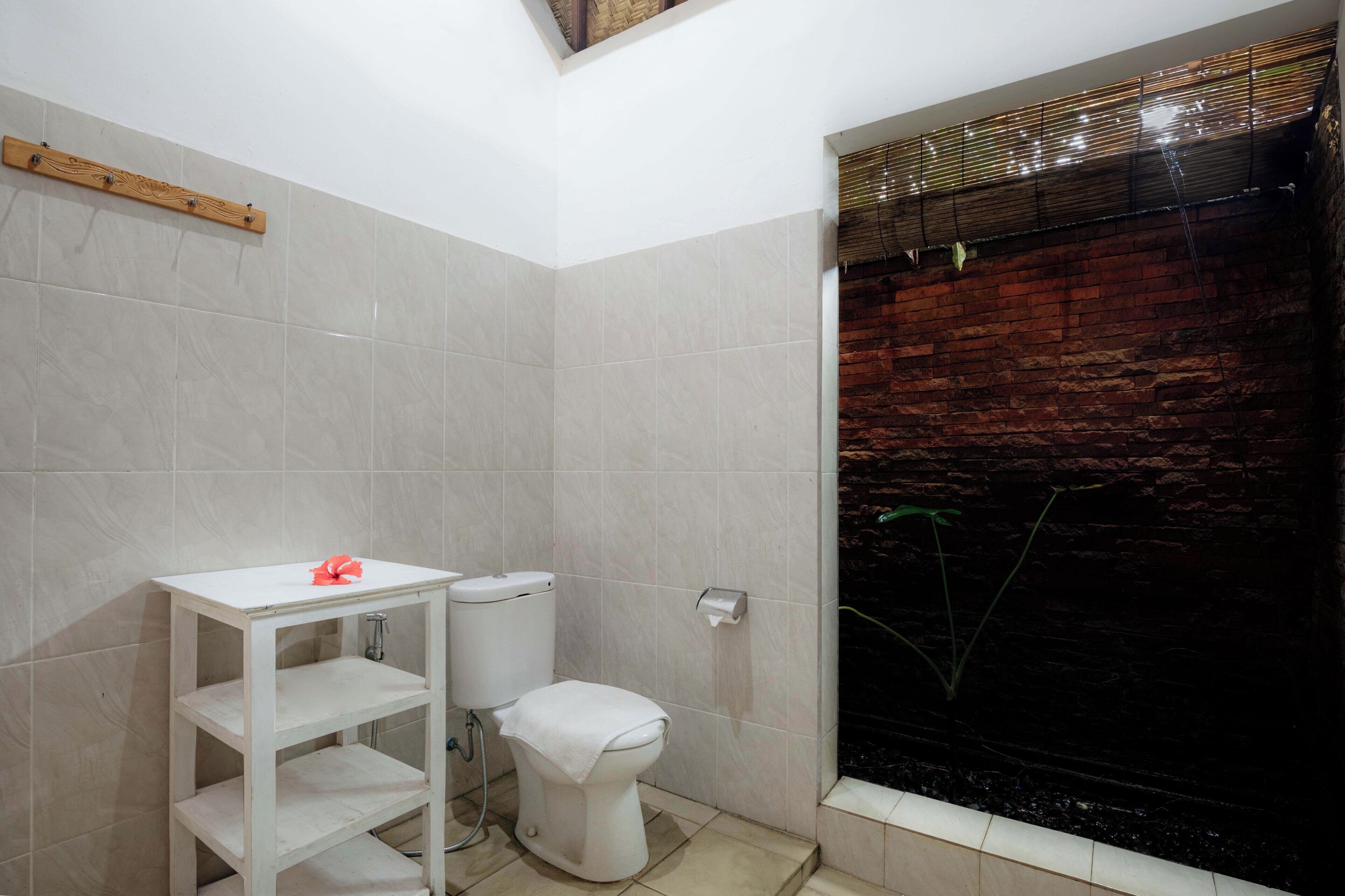Un baño con inodoro, repisa y zona de ducha con pared de ladrillo.