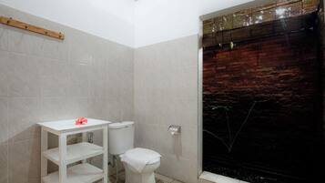 Un baño con inodoro, repisa y zona de ducha con pared de ladrillo.