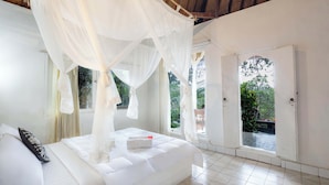 A bedroom with a canopy bed, white bedding, and a view of the outdoors through a door. - Taman Indrakila (Ubud)