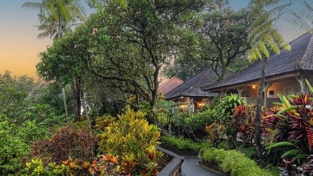 A pathway leading to a traditional-style building surrounded by lush greenery and flowering plants. - Taman Indrakila (Ubud)