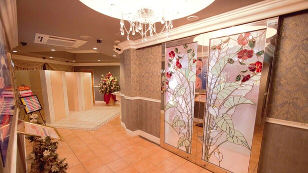 A hotel lobby with a tiled floor, a chandelier, a floral arrangement, and a glass partition with a floral design. - Hotel LaLa PAT1 - Adults Only (Sakai)
