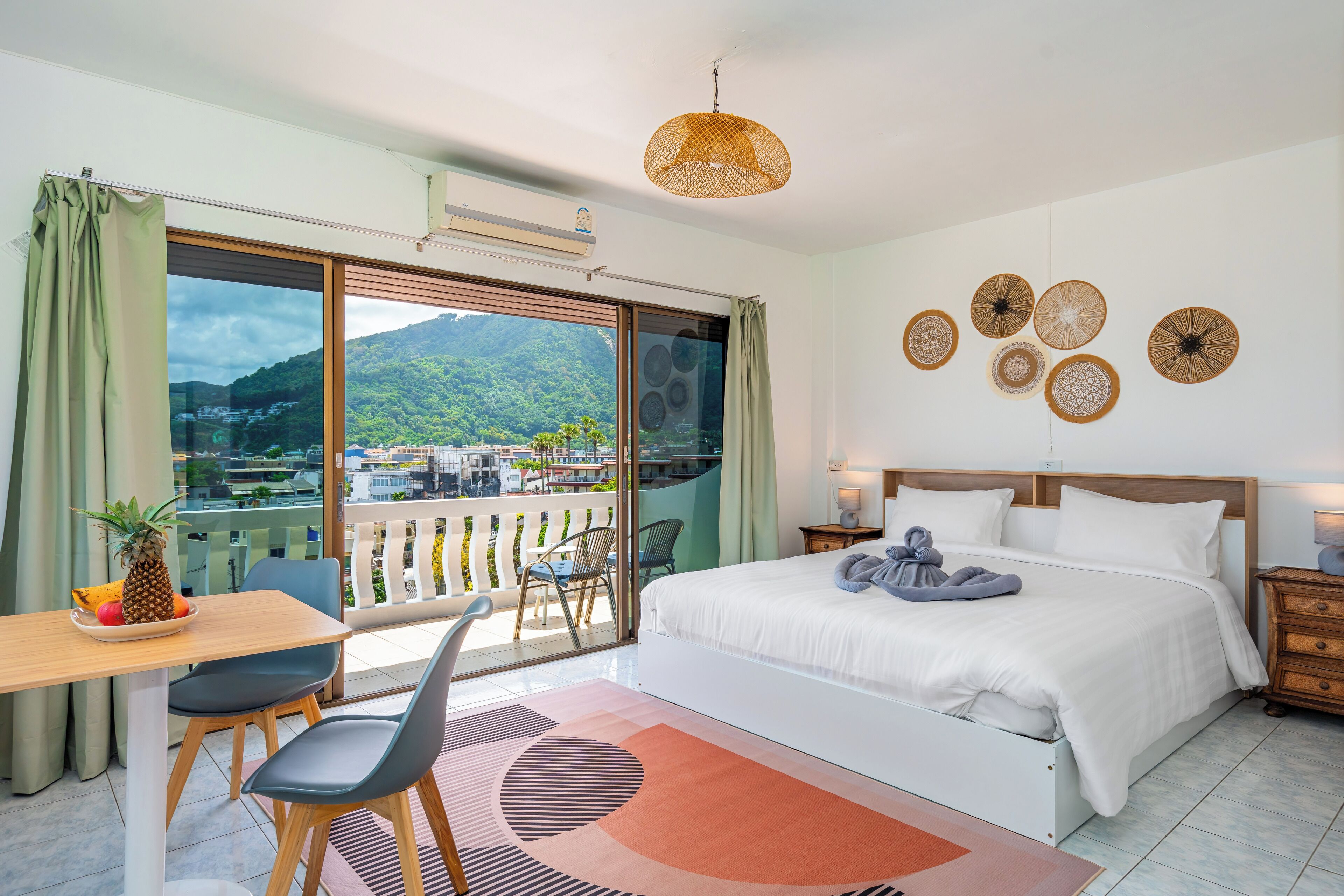 A modern hotel room with a large bed, a balcony with a view of the mountains, a dining area with a table and chairs, and decorative wall art.