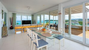 A spacious living area with a glass dining table, comfortable seating, and a large TV.