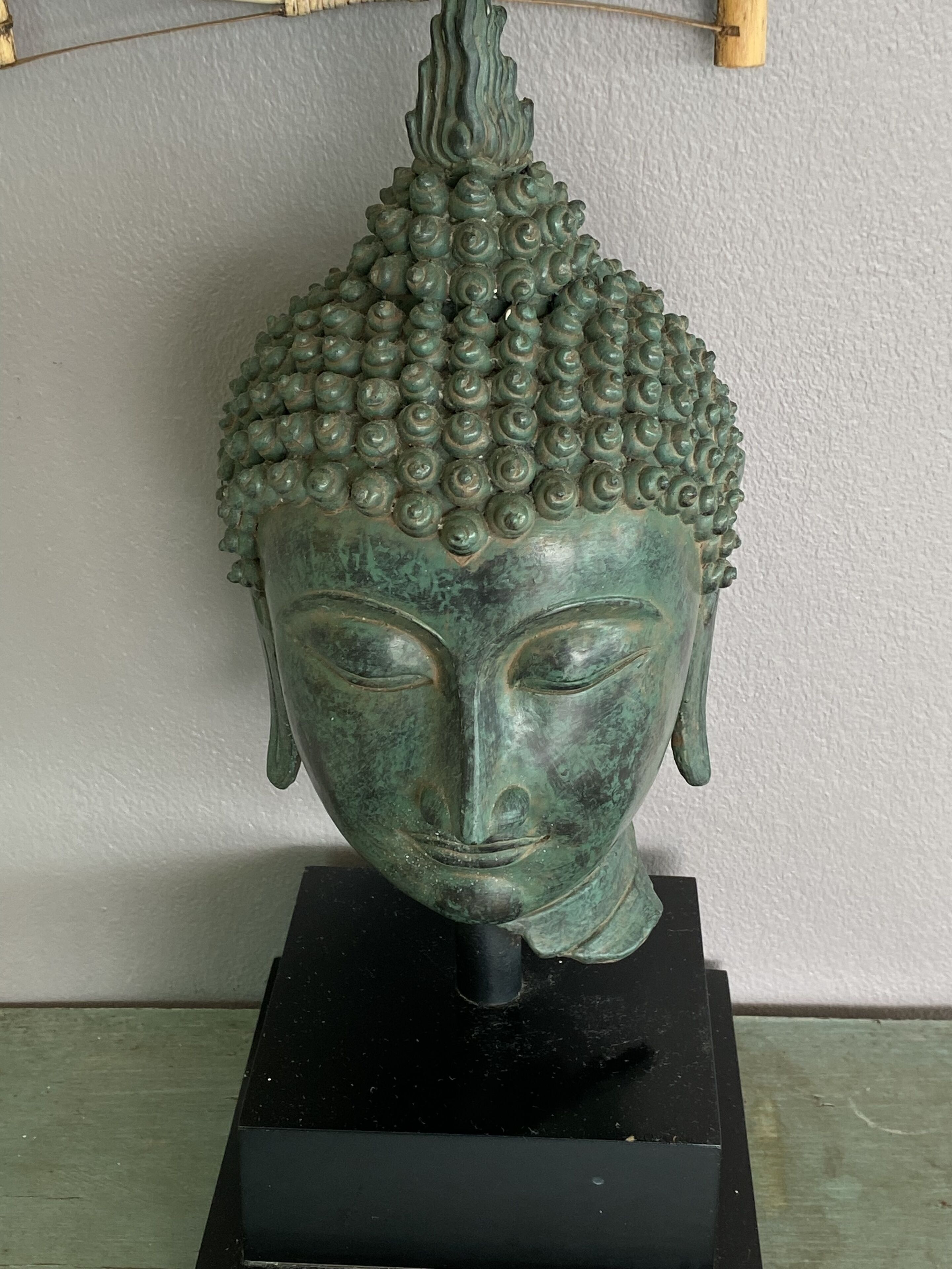 Una escultura de cap de Buda de bronze sobre un pedestal negre.