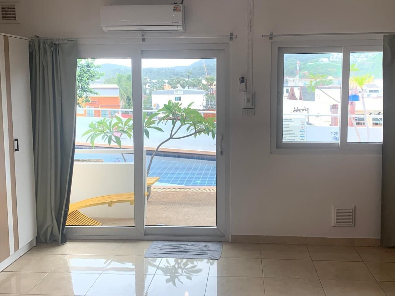 A room with a sliding glass door leading to a balcony with a pool and solar panels.