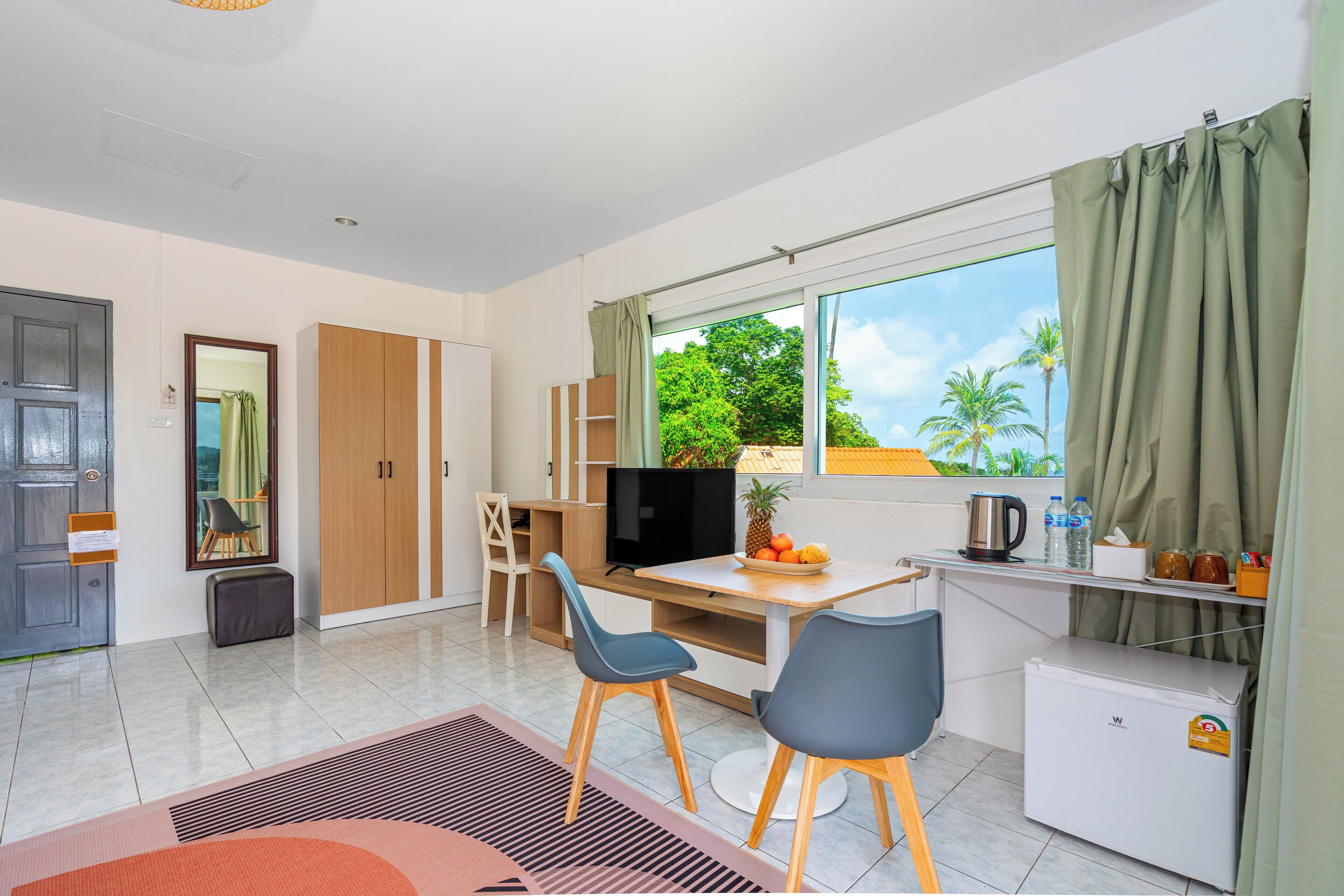 Un espacio habitable compacto con kitchenette, comedor, televisor y ventana con cortinas.