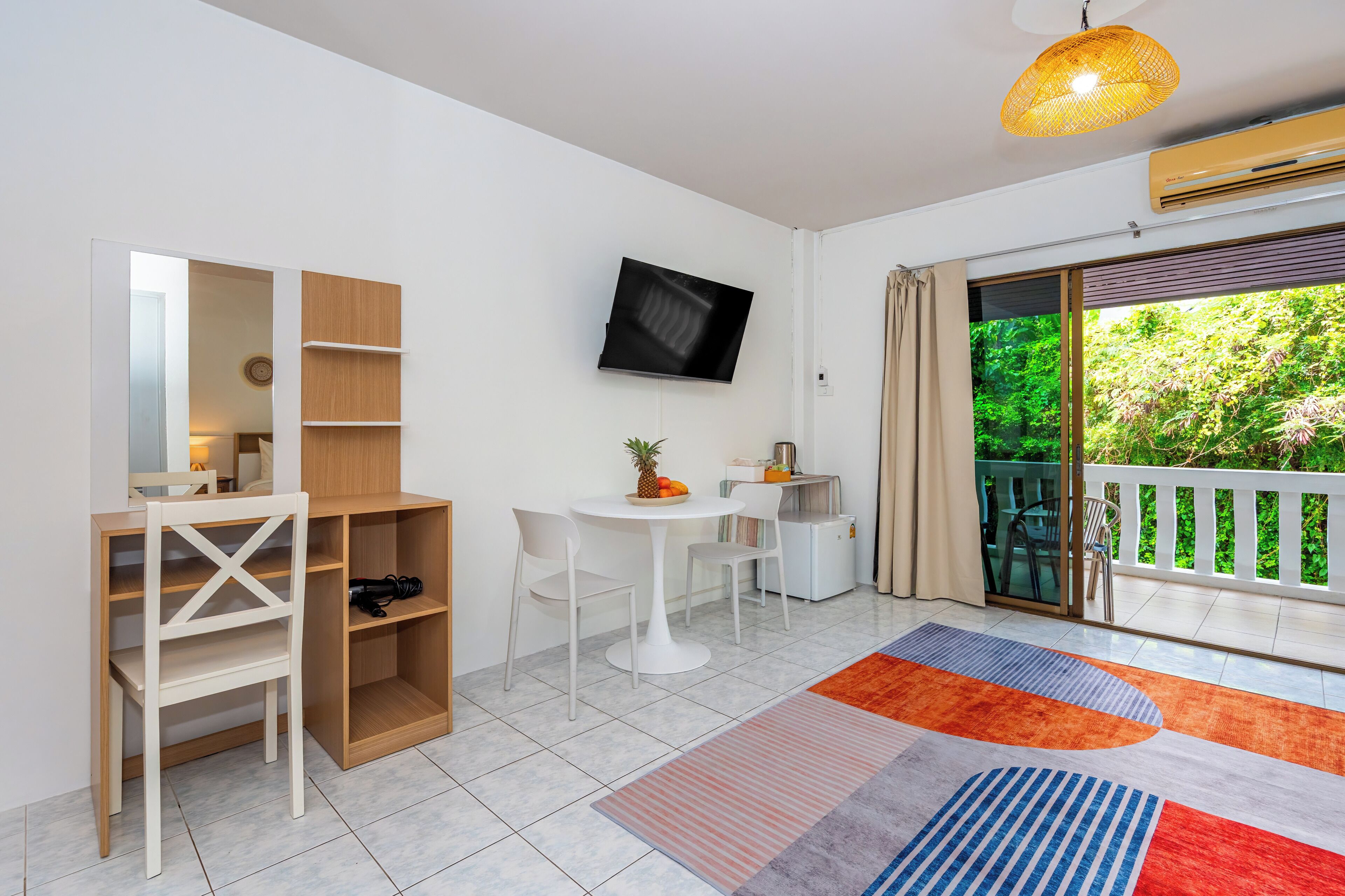 A modern room with a desk, chairs, a TV, and a balcony with a view of greenery.
