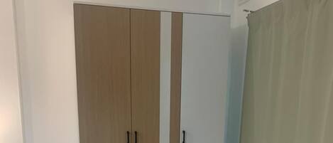 Habitación con armario de dos puertas, una con detalles de madera y la otra blanca. El piso es de baldosas y hay una cortina a la derecha.