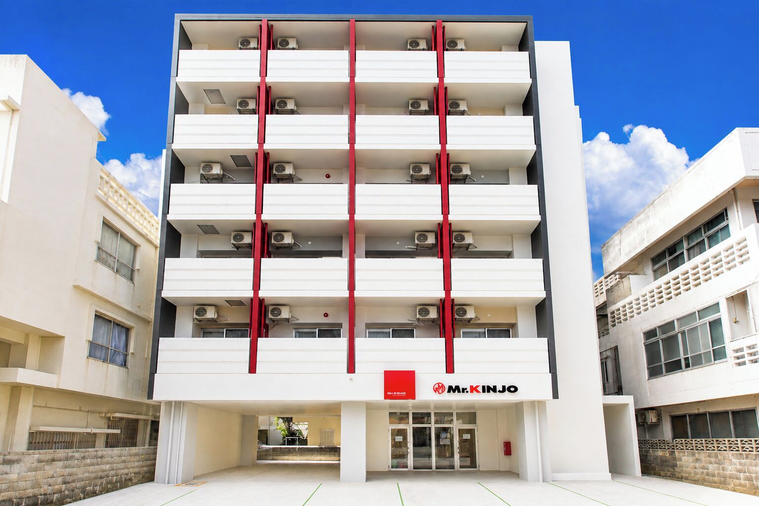 A multi-story building with a central red vertical feature, air conditioning units on each floor, and a sign reading 'Mr. KINJO' at the entrance.
