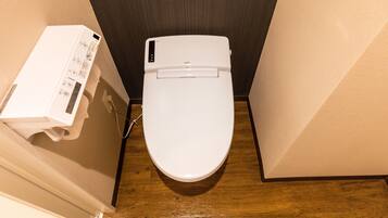 Inodoro blanco con panel de control, suelo de madera y pared oscura.