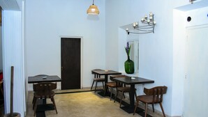 A narrow hallway with a dining area featuring tables and chairs, a green vase with flowers, and a wall-mounted light fixture. - Rohoney Boutique Villa (Galle)