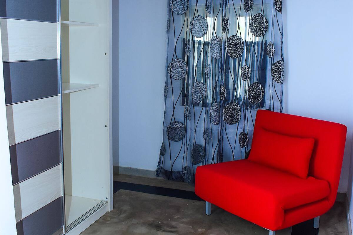Une petite pièce fermée, avec un canapé rouge, une porte-fenêtre coulissante et un rideau à motifs.
