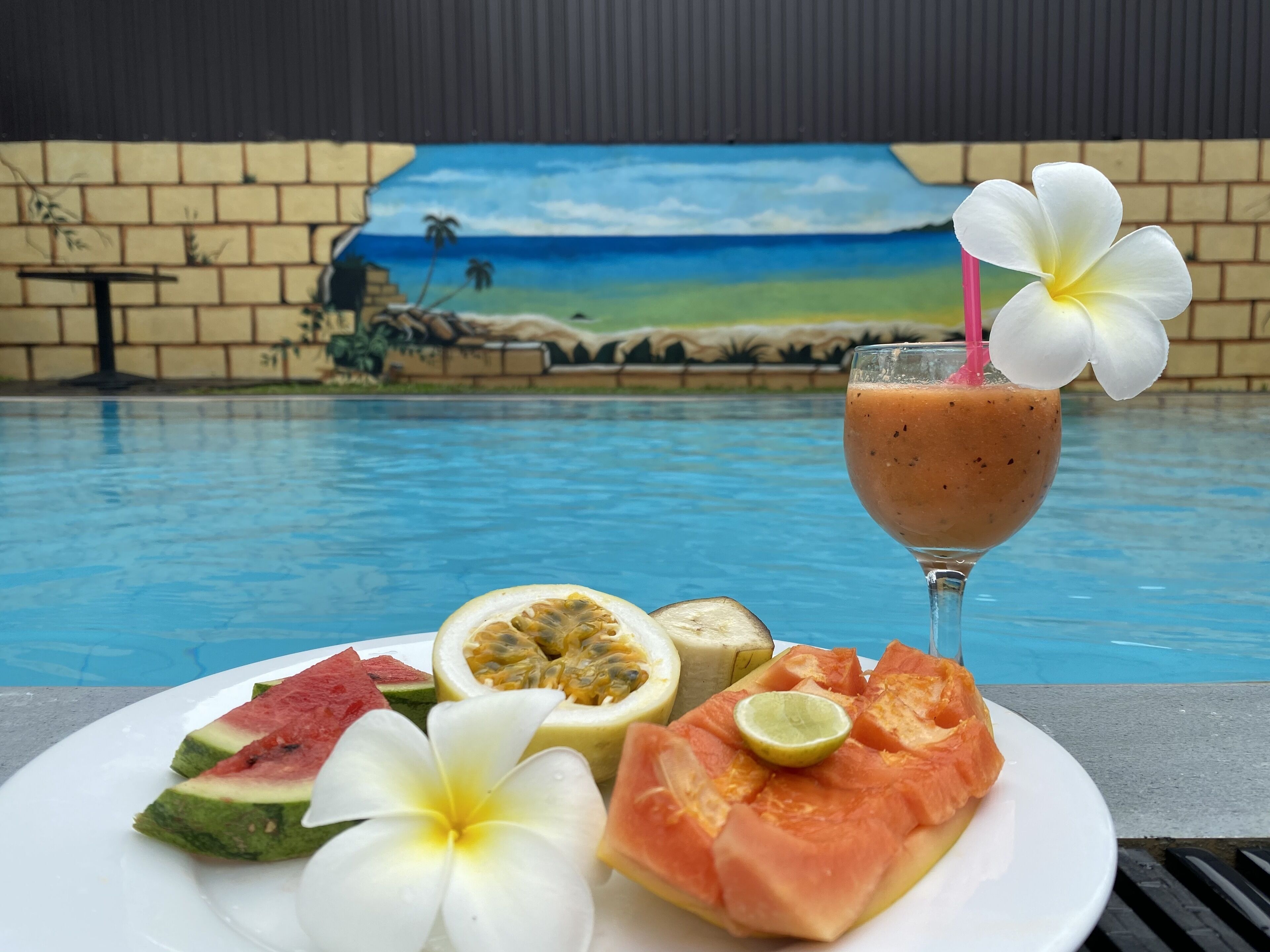 A dining table with a plate of food and a drink by a pool.