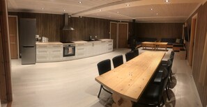 A modern kitchen with a central island, a dining area with a long wooden table, and a built-in seating area. - Skeikampen Appartement (Gausdal)