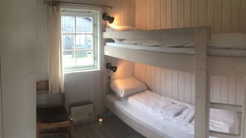 A room with bunk beds, a window with curtains, a chair, and a wall-mounted lamp.