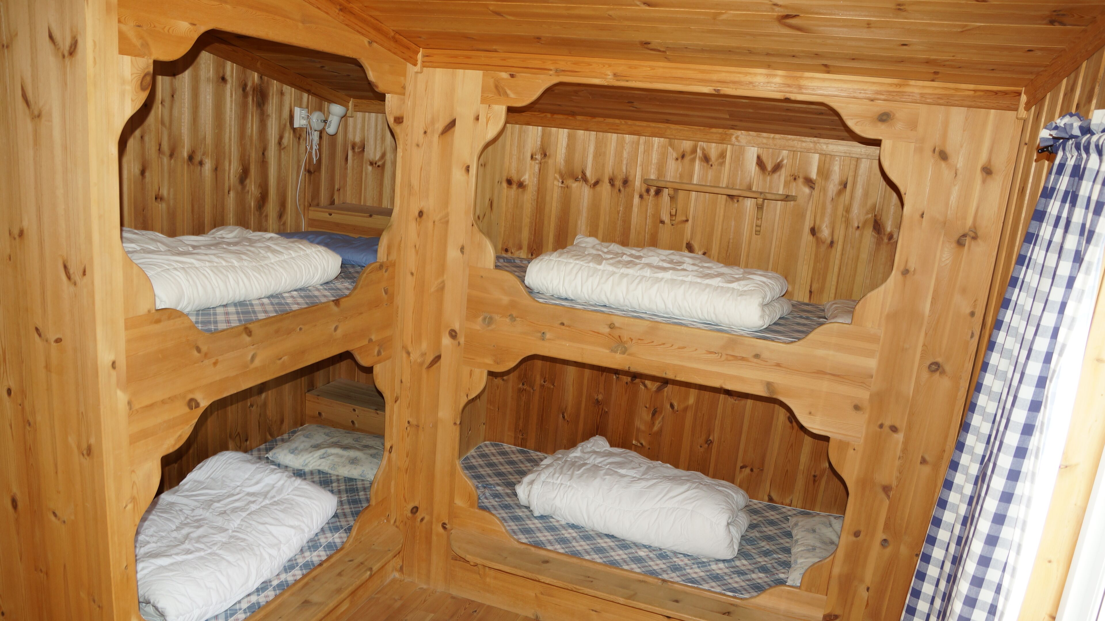 Une cabane en bois avec quatre lits superposés, chacun doté d’un matelas à carreaux et de draps blancs.